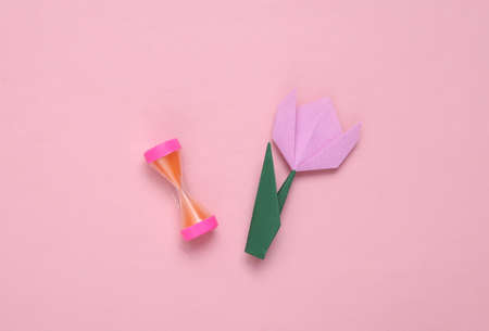 Hourglass and origami tulip on pink background