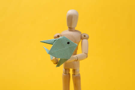 Wooden puppet holding origami fish on yellow backgroundの写真素材