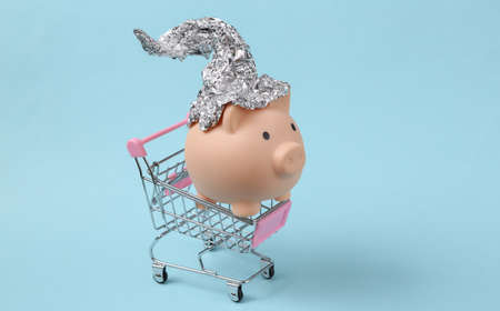 Piggy bank with foil hat in shopping trolley on blue backgroundの写真素材