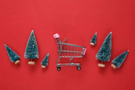 Mini Christmas trees and shopping trolley on red background. new year or christmas backgroundの写真素材