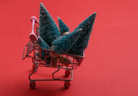 Mini supermarket cart with christmas trees on red backgroundの写真素材