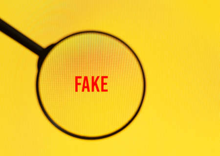 Word fake on yellow screen through magnifying glass.の写真素材