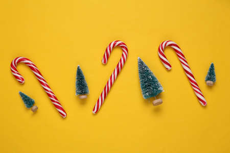 Christmas striped candy canes and mini Christmas trees on yellow background. new year, xmas...