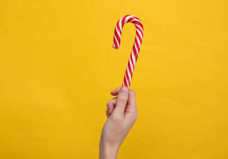 Hand holding Christmas striped candy cane on yellow background.の写真素材