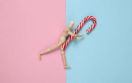 Wooden puppet holding Christmas striped candy cane on a blue pink background.の写真素材