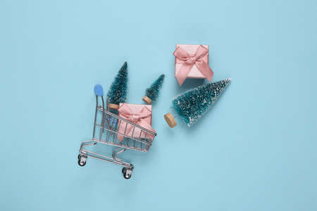 Mini supermarket cart with christmas trees, gift boxes on blue backgroundの写真素材