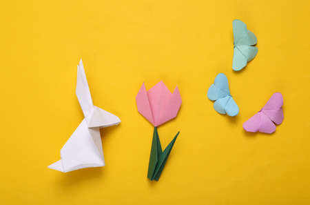 Easter composition of origami tulips, rabbit and butterflies, eggs on a yellow background