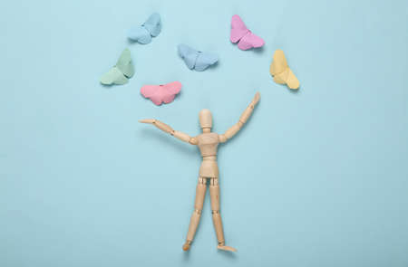 Wooden happy puppet and origami butterflies on a blue background