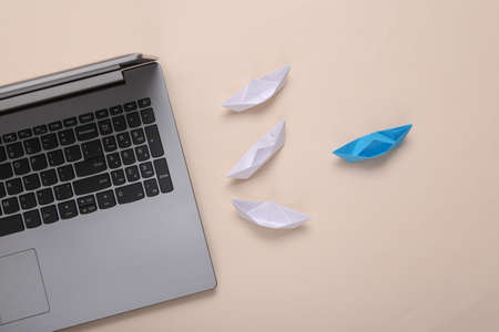 leadership concept. Laptop and Origami paper boats on beige backgroundの写真素材