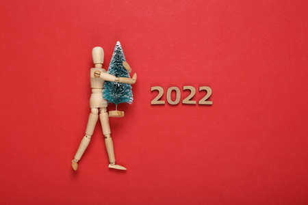 2022 and wooden puppet holding mini christmas tree on red background. Christmas, new year compositionの写真素材