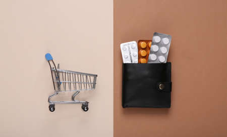 Mini supermarket trolley and purse with blister of pills on brown beige backgroundの写真素材