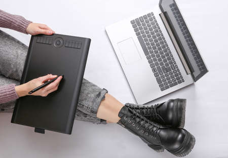 Woman works with a graphics tablet on a white background. Female legs in jeans and boots....