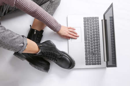 The woman uses a laptop on a white background. Female legs in jeans and boots. Online work. top viewの写真素材