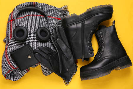 Women's accessories. Black Leather boots, scarf, headphones, wallet and gloves on yellow background. top view. flat layの写真素材