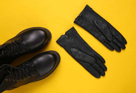 Women's accessories. Black Leather boots, gloves on yellow background. top view. flat layの写真素材