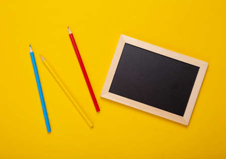 Mini blackboard and color pencils on yellow background. Empty, blank chalkboard with copy space....
