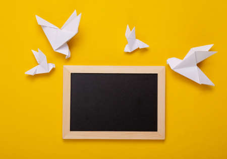 Mini blackboard and origami doves on yellow background. Empty, blank chalkboard with copy space.の写真素材