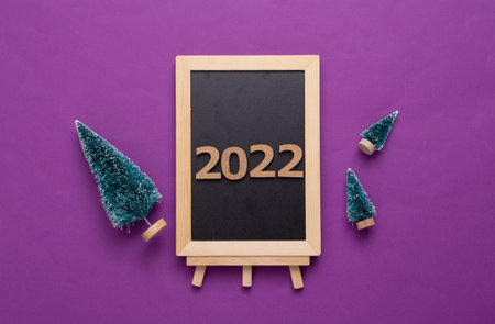 Mini blackboard with Christmas tree on purple background. Chalkboard with 2022. New year, Christmas still lifeの写真素材