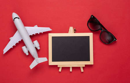Blank mini chalkboard with copy space and airplane with sunglasses on red background. Travel, trip...