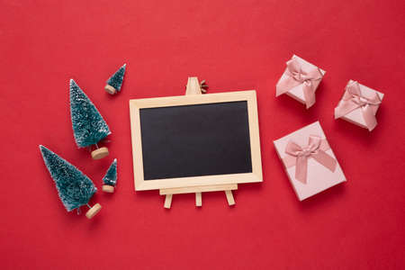 Mini blackboard with Christmas tree, gift boxes on red background. Empty, blank chalkboard with copy space. New year, Christmas still lifeの写真素材