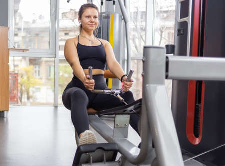 Fit woman trains back muscles in cable rowing exercise machine in the gym