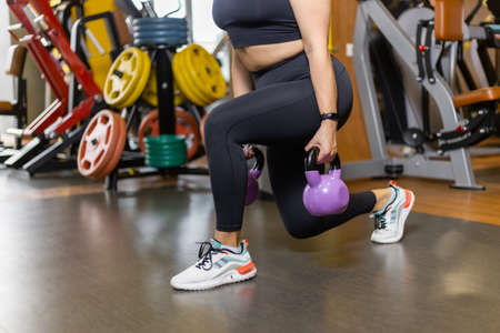 Fit woman practices lunges with kettlebells in her hands in the gym. Leg workout