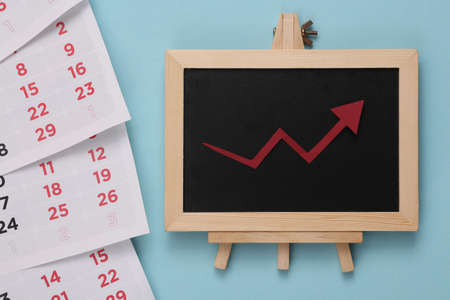 Mini chalk board with a growth arrow and calendar on blue background. business conceptの写真素材