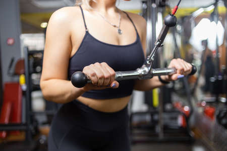Young attractive sport woman trains triceps in crossover cable exercise machine in gym