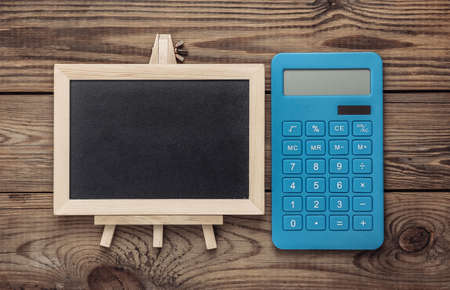 Mini blackboard and calculator on wooden table. Empty, blank chalkboard with copy space. Business, education, learning concept.の写真素材