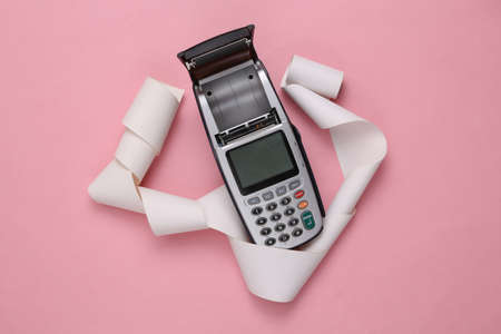 Open payment terminal with paper tape on pink background