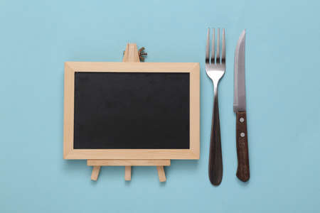 Empty mini chalk board, knife and fork on a blue background. restaurant menuの写真素材