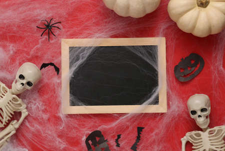 Mini blank chalk board with copy space and halloween decor with cobwebs on red background. Trick or...