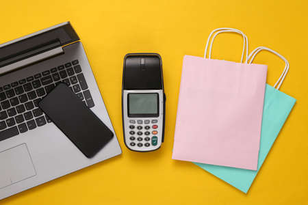 Payment terminal with smartphone, bags and laptop on yellow background. Payment for purchases. online shopping. top viewの写真素材