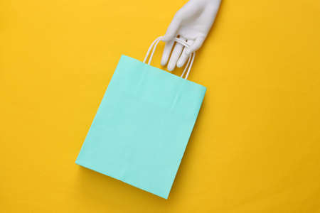 Mannequin hand holding paper shopping bag on yellow backgroundの写真素材
