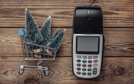 Payment terminal and mini Christmas trees in shopping trolley on wooden table. Christmas shopping. top viewの写真素材