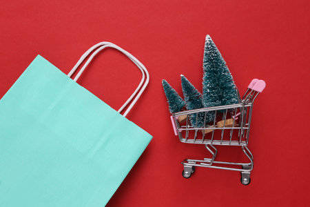 Shopping bag, shopping trolley with mini Christmas trees on red background.の写真素材