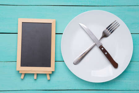 Plate with fork and knife, empty mini chalk board on blue wooden background. Restaurant menu. copy spaceの写真素材