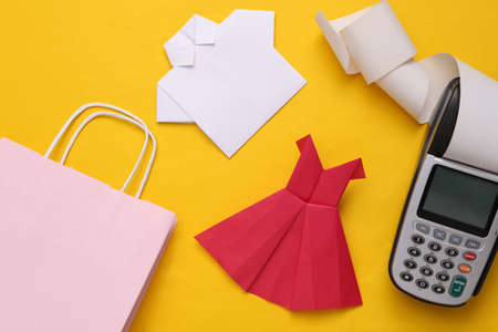 Shopping bag with origami dress and shirt, payment terminal on a yellow background. Payment for...