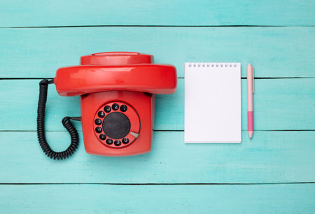 Retro red old fashioned rotary phone and notebook on blue wooden table. top viewの写真素材