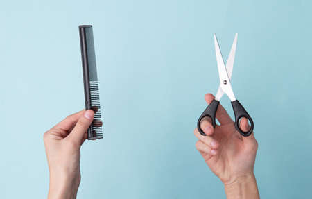 Hand holding scissors and hairbrush on blue background. Set for haircuts, hair care, barbershop