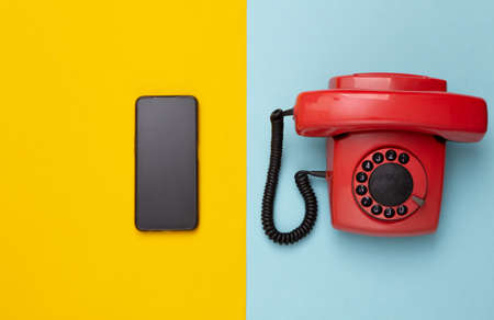 Retro red old fashioned rotary phone and modern smartphone on yellow blue background. top viewの写真素材