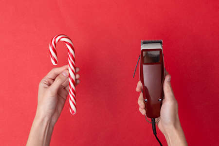 Hand holding Machine for hairstyle (Hair clippers) and candy cane on red background. Barbershop.の写真素材
