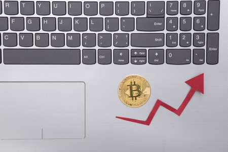 Laptop, Bitcoin and growth arrow on gray background. Cryptocurrency. The rise in the value of...