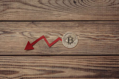 Fall arrow and golden bitcoin on a wooden table. falling bitcoin priceの写真素材