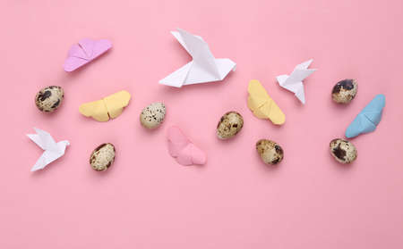 Quail eggs and origami butterflies, doves on pink pastel background. Easter composition. top view