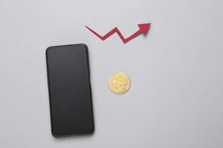 Cryptocurrency trading. The rise price of bitcoin. Gold bitcoin coin, smartphone and growth arrow on gray backgroundの写真素材