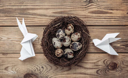 Easter composition. Origami Easter bunny and doves, quail eggs in nest on wooden table. top view