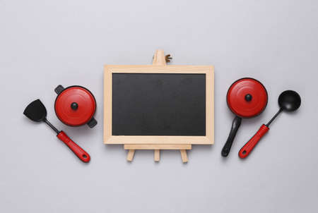 Toy kitchen pots and tools, empty chalk board on gray background. Cooking concept. copy spaceの写真素材