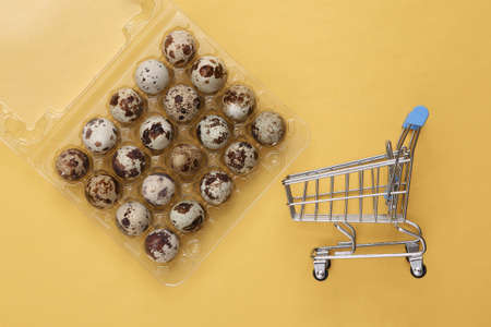 Tray with quail eggs and mini supermarket trolley on yellow background. top viewの写真素材
