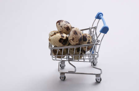 Mini supermarket cart with quail eggs on a gray background.